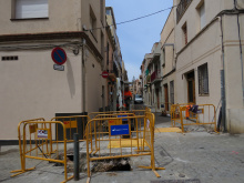 Carrer de Massevà amb operari fent anar una excavadora i rasa protegida amb tanques d'obres en primer pla