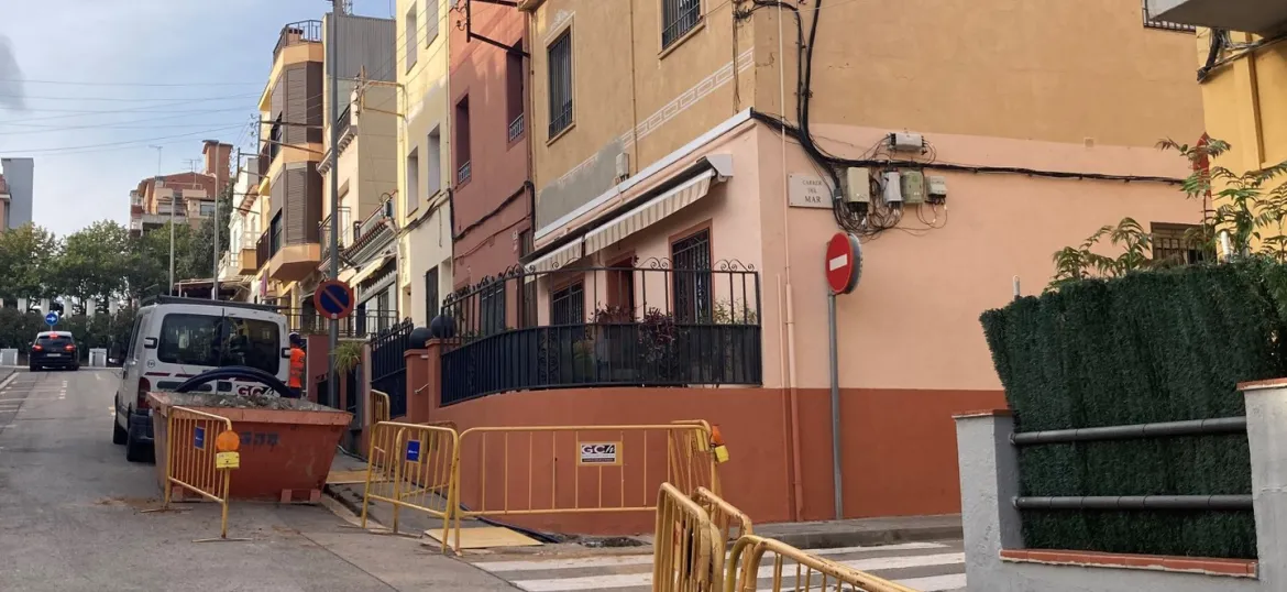 Carrer amb dues tanques d'obres en primer pla i contenidor d'obres